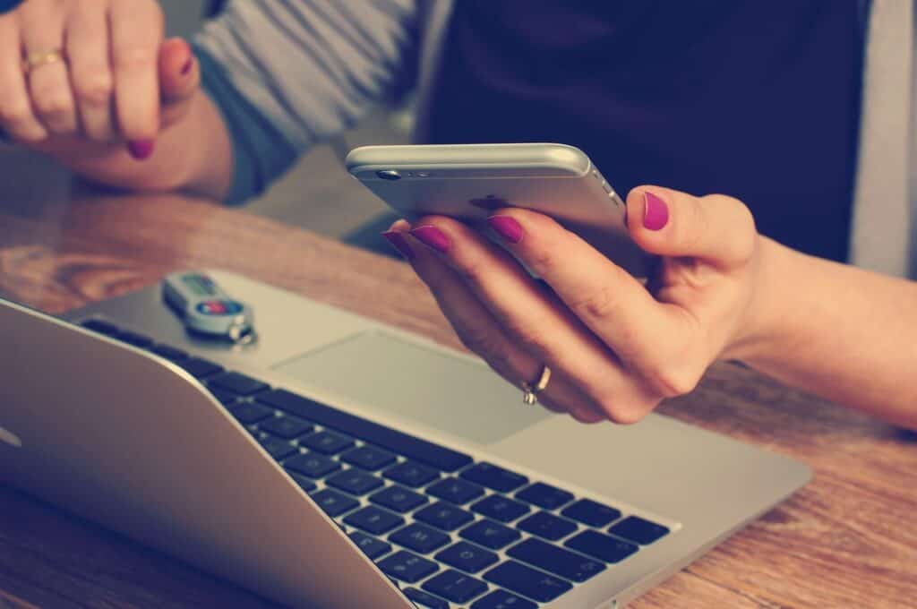woman's hands with wedding ring holding phone in front of computer