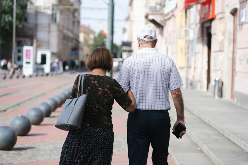 older couple backs walking arm in arm down street
